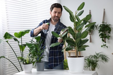 Photo of Man spraying beautiful potted houseplants with water indoors