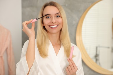 Beautiful happy woman applying mascara in bathroom