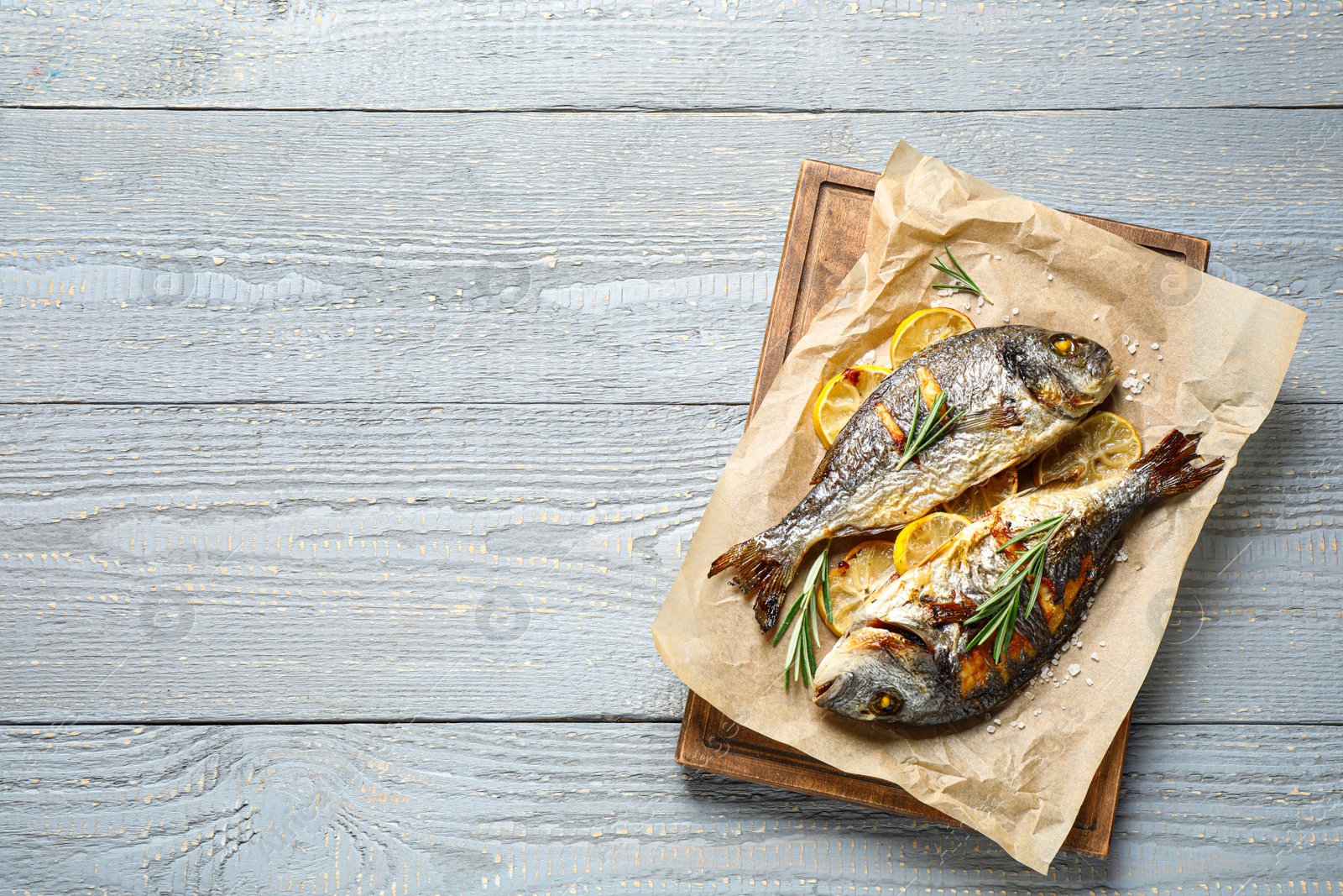 Photo of Delicious roasted fish with lemon on grey wooden table, flat lay. Space for text