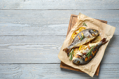 Photo of Delicious roasted fish with lemon on grey wooden table, flat lay. Space for text