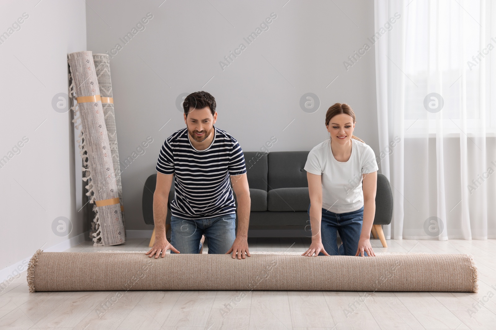 Photo of Smiling couple unrolling carpet on floor in room