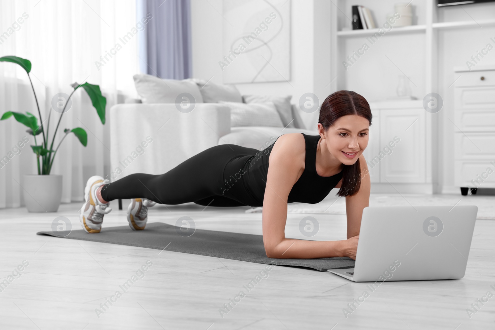 Photo of Happy woman doing plank exercise and watching video tutorial via laptop at home