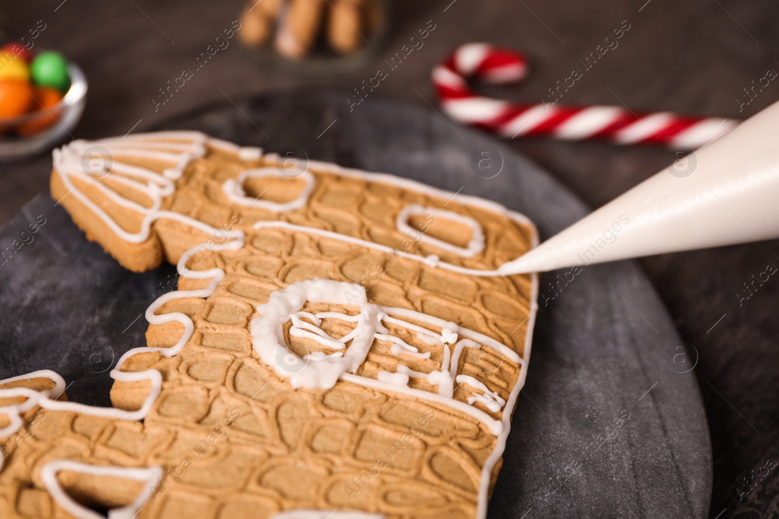 Photo of Decorating gingerbread house part with icing on grey board, closeup