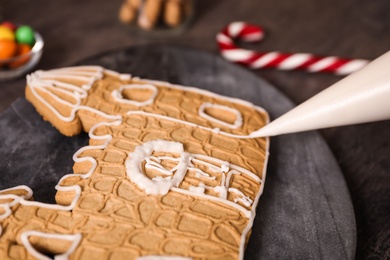Photo of Decorating gingerbread house part with icing on grey board, closeup