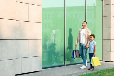 Photo of Family shopping. Happy father and son with colorful bags near mall outdoors