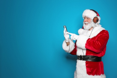 Santa Claus listening to Christmas music on color background