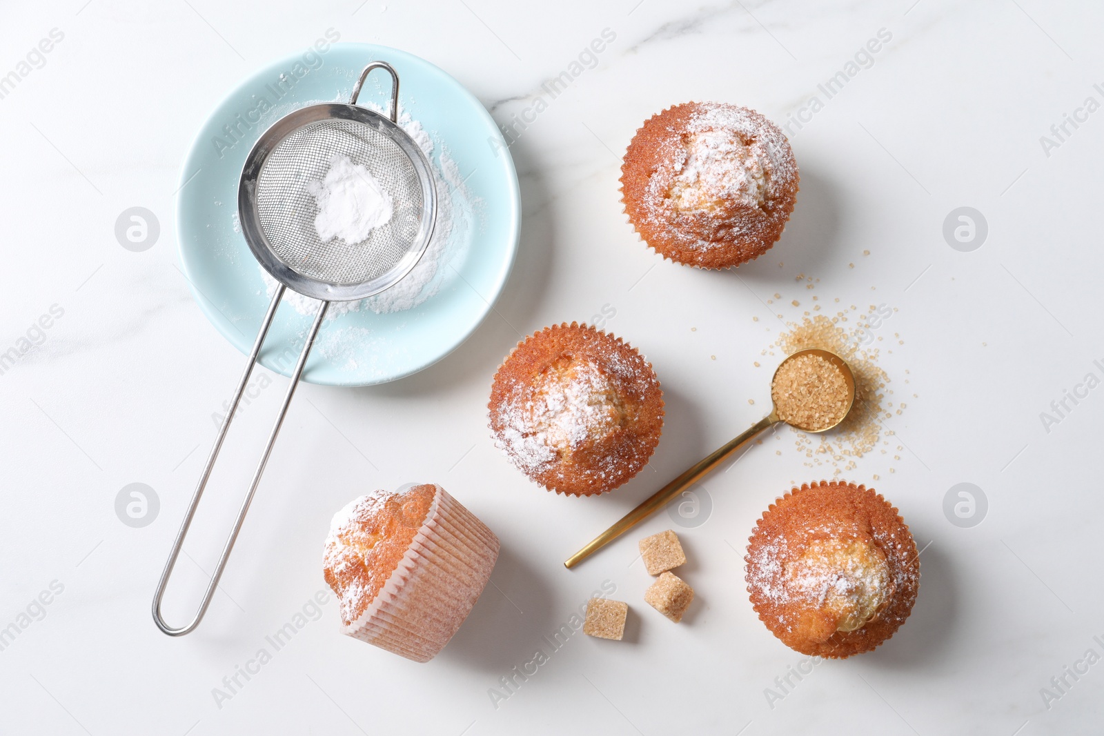 Photo of Delicious sweet muffins, plate and sieve on white marble table, flat lay