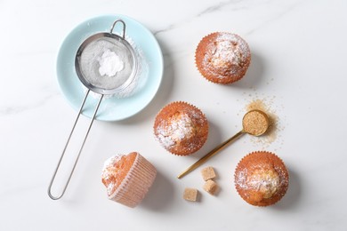 Delicious sweet muffins, plate and sieve on white marble table, flat lay