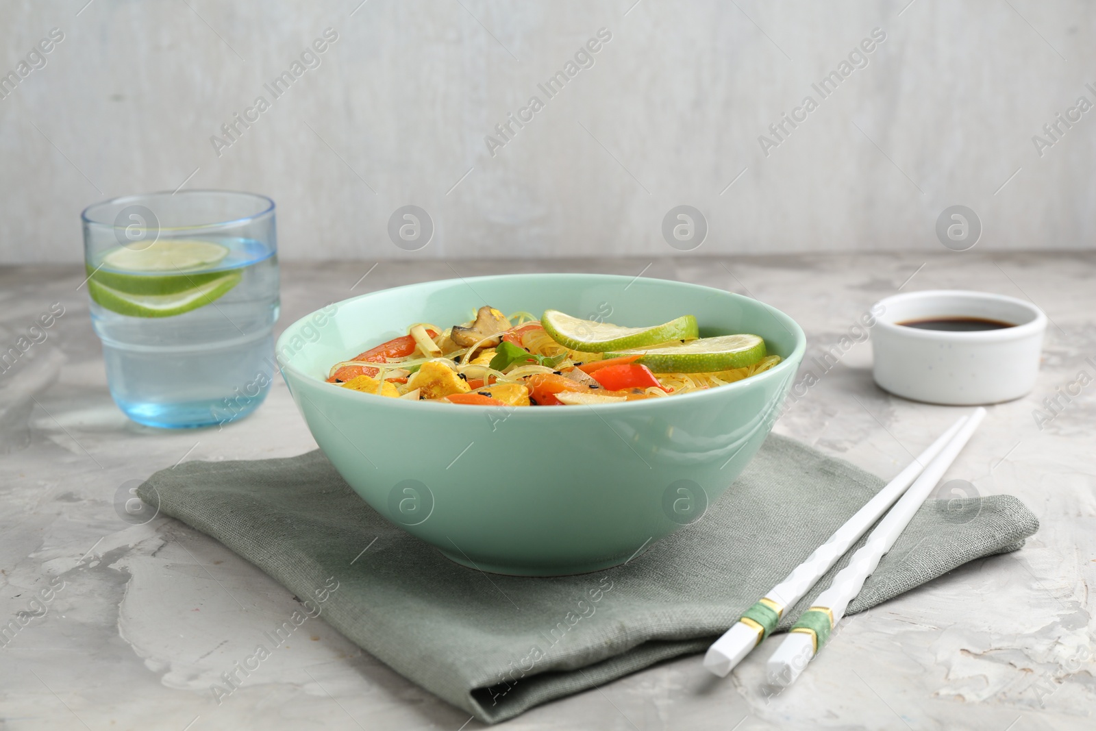 Photo of Stir-fry. Delicious cooked noodles with chicken and vegetables in bowl served on gray textured table