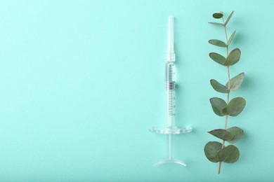 Photo of Cosmetology. Medical syringe and eucalyptus branch on turquoise background, flat lay. Space for text