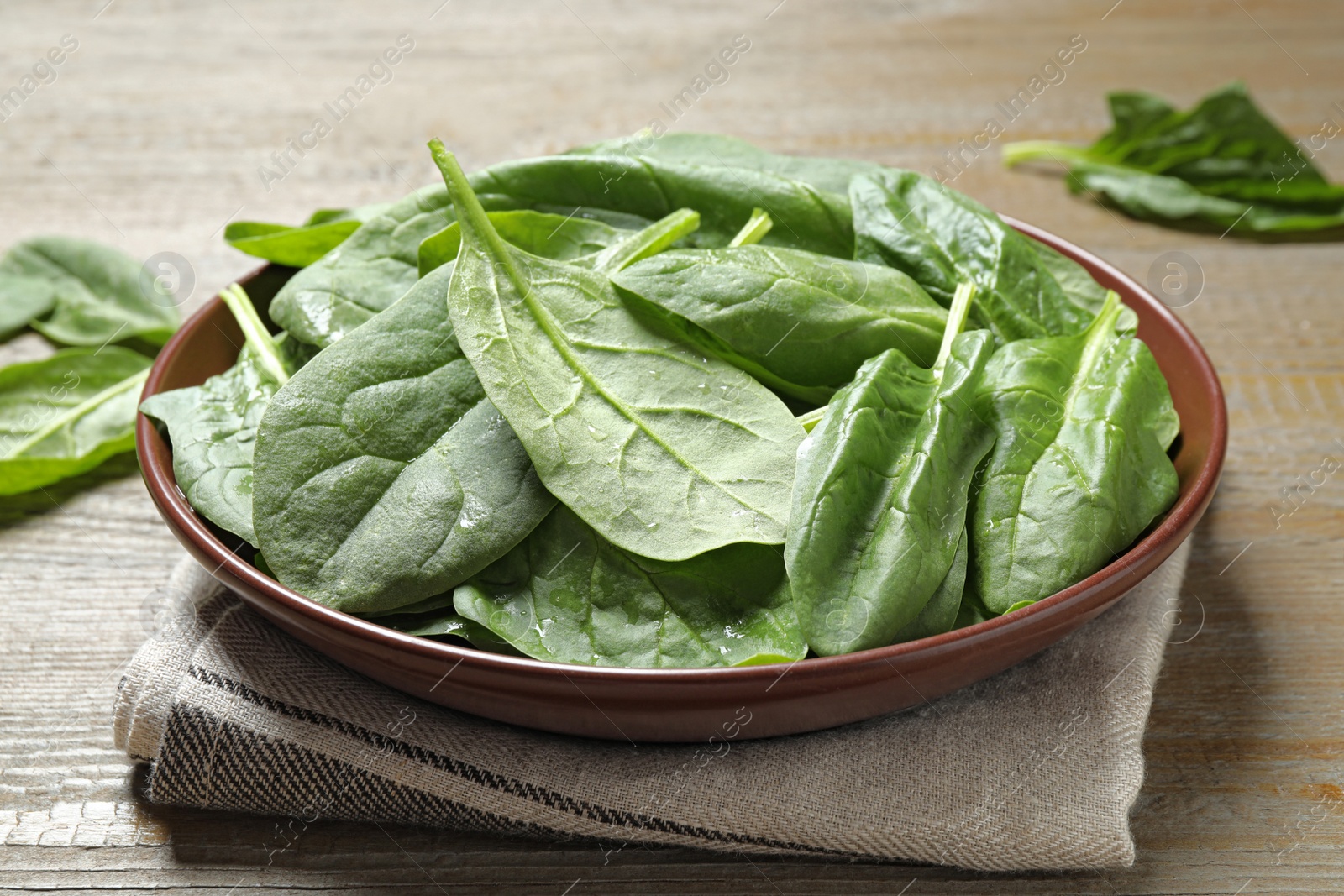 Photo of Bowl with fresh green healthy spinach on wooden table