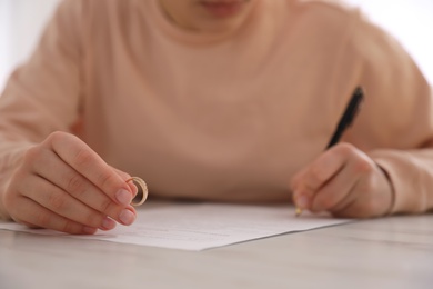 Photo of Woman with wedding ring signing divorce papers at table, closeup