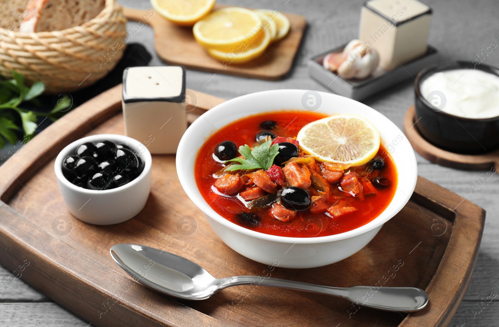 Photo of Meat solyanka soup with sausages, olives and vegetables in bowl served on grey table