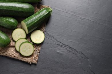 Photo of Whole and cut ripe zucchinis on black table, flat lay. Space for text