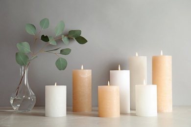 Photo of Composition with burning candles on table against light background