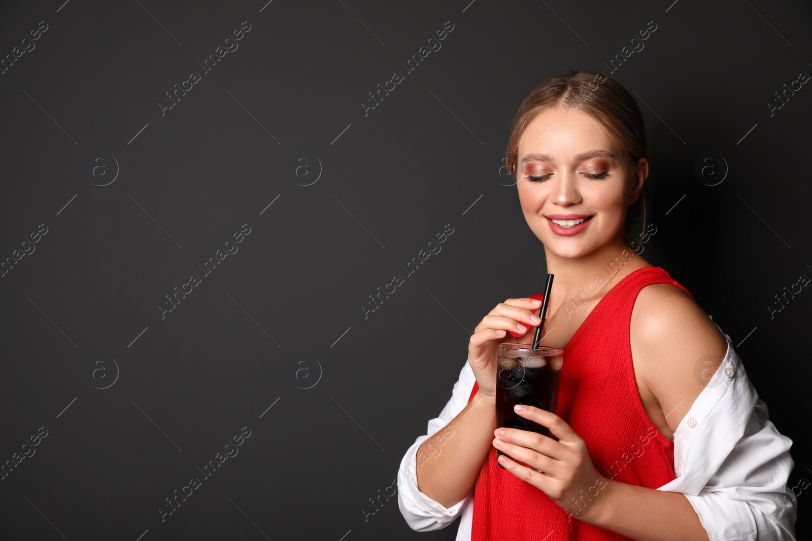 Photo of Young woman with glass of cola on black background, space for text. Refreshing drink