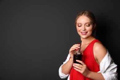 Young woman with glass of cola on black background, space for text. Refreshing drink