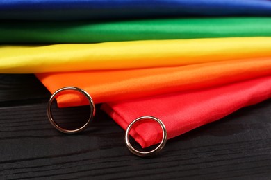 Photo of Rainbow LGBT flag and wedding rings on black wooden background