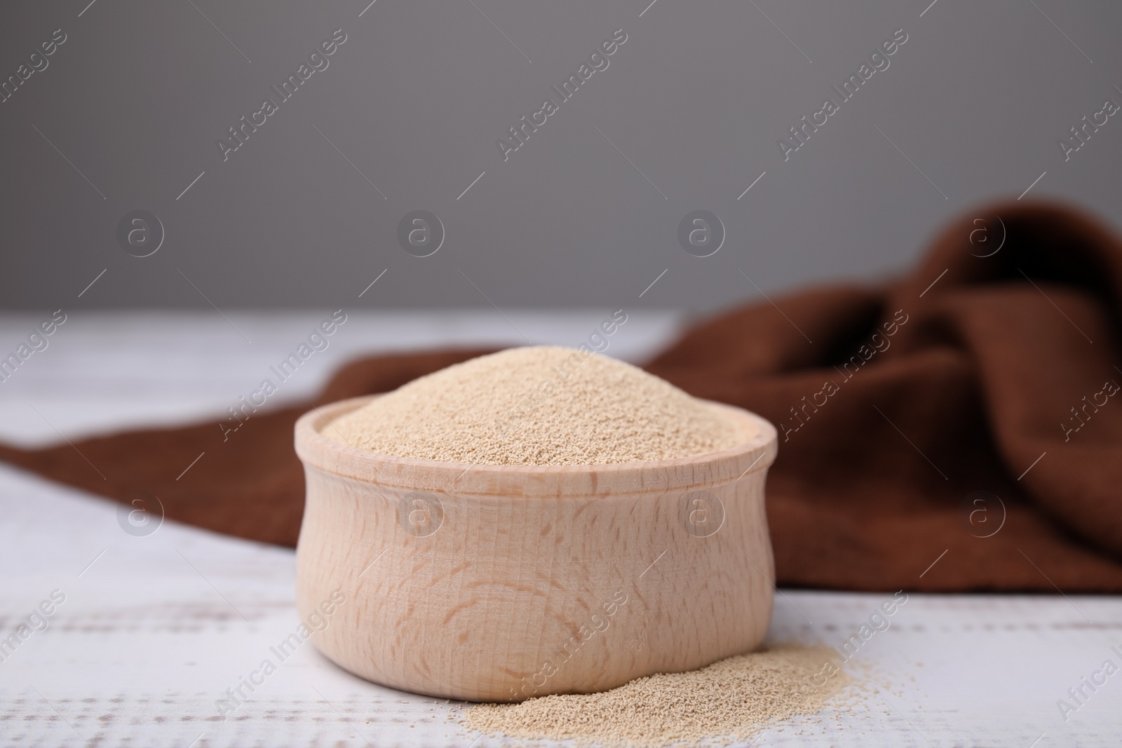 Photo of Granulated yeast in bowl on white wooden table, closeup