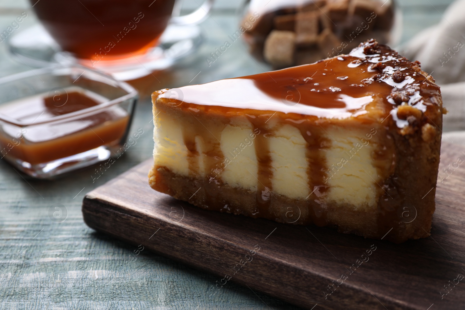 Photo of Piece of delicious cake with caramel served on blue wooden table, closeup