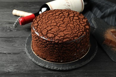 Photo of Delicious truffle cake, bottle of wine, chocolate pieces and corkscrew on black wooden table