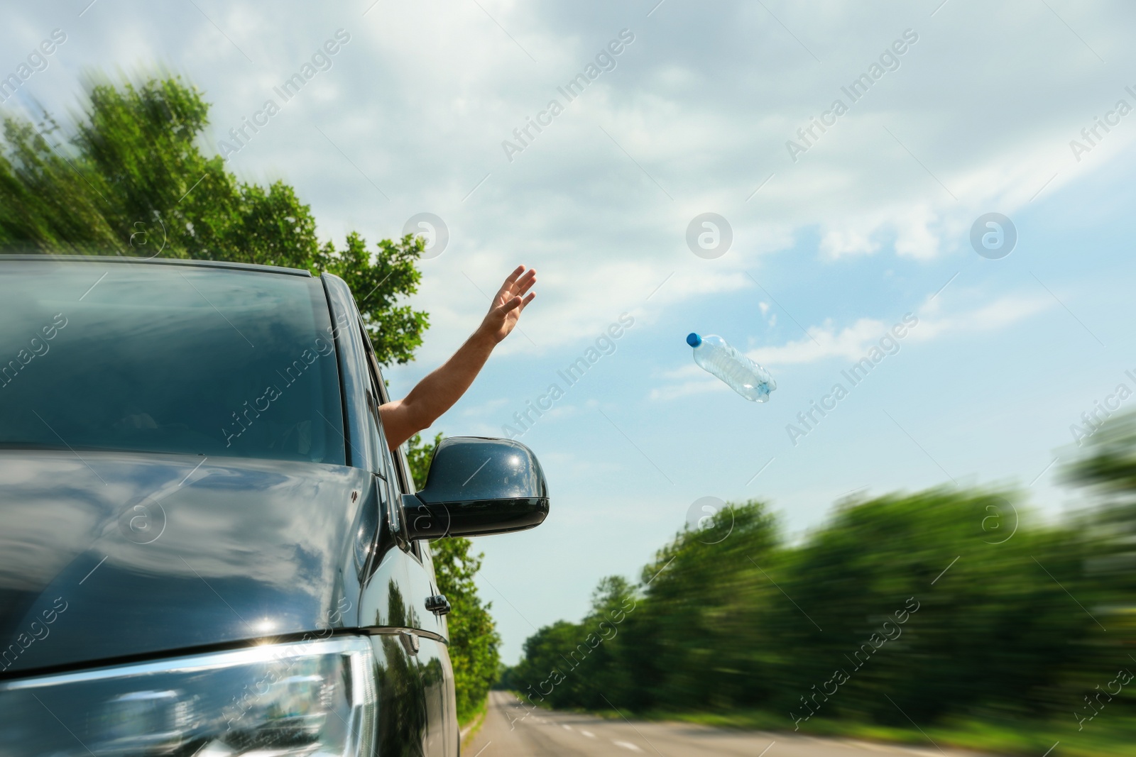 Photo of Driver throwing away plastic bottle from car window. Garbage on road