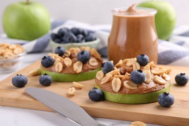 Slices of fresh apple with peanut butter, blueberries and nuts on white table, closeup
