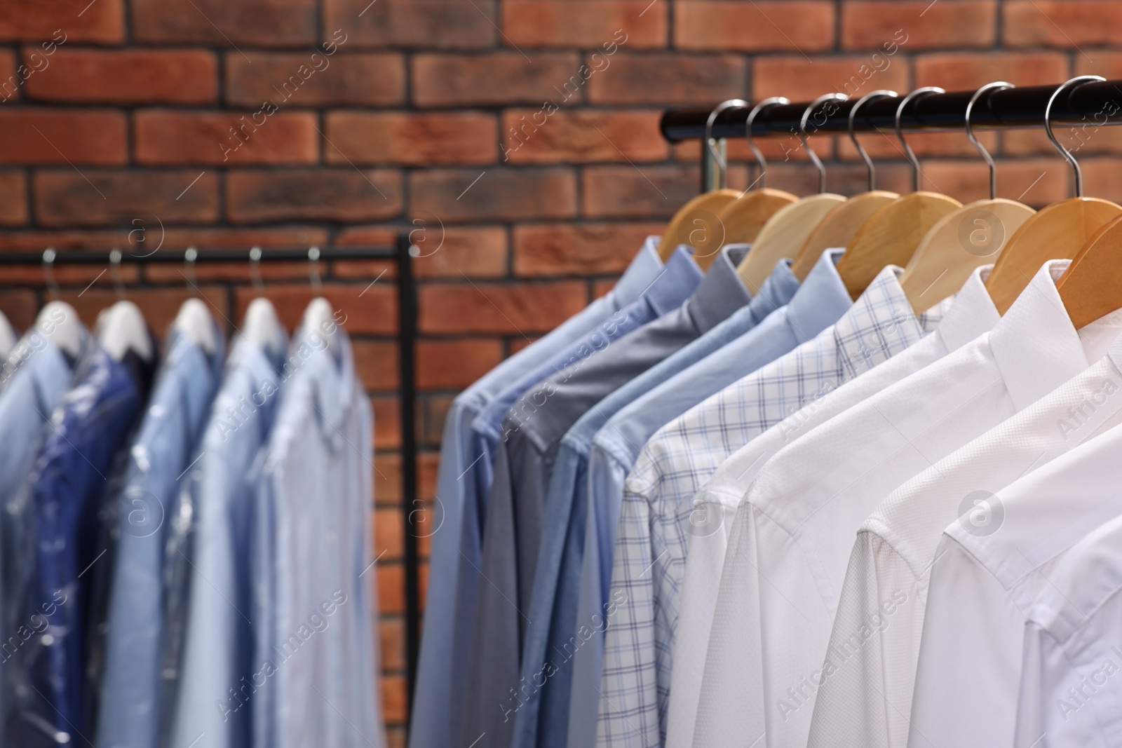 Photo of Dry-cleaning service. Many different clothes hanging on rack against brick wall, closeup