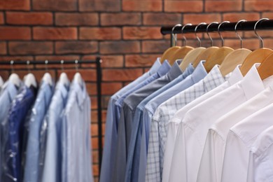 Dry-cleaning service. Many different clothes hanging on rack against brick wall, closeup