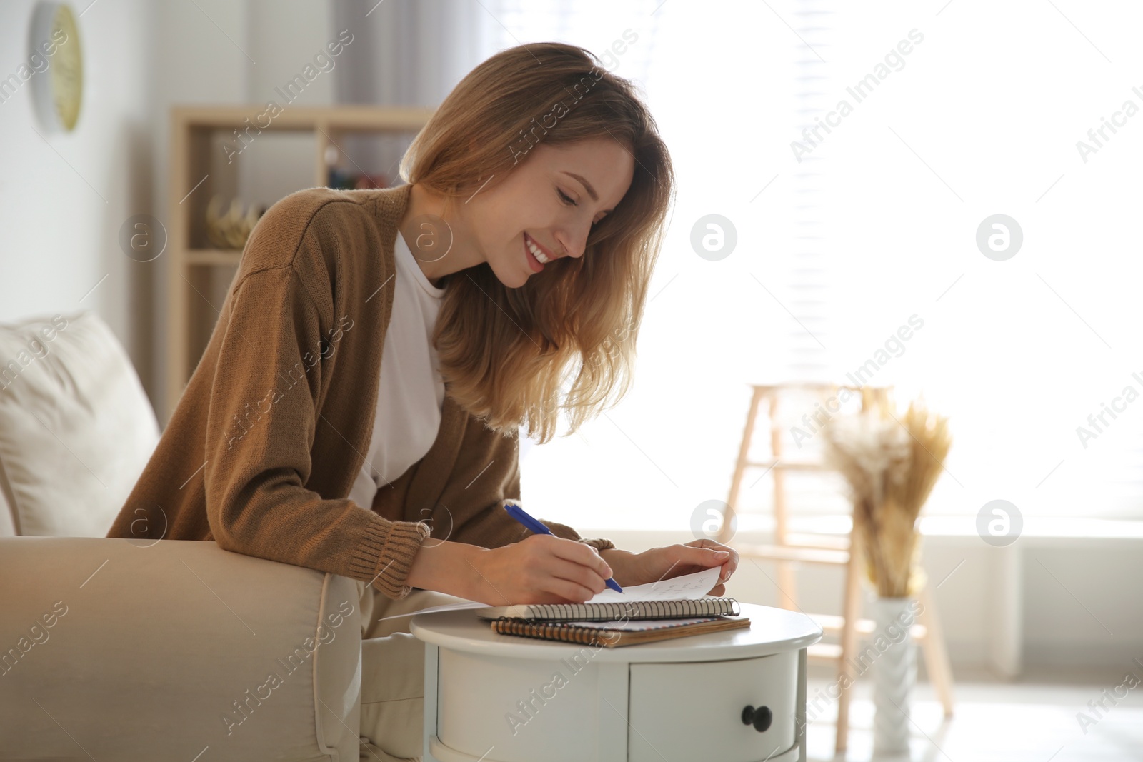 Photo of Happy woman writing letter at table in living room