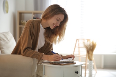 Happy woman writing letter at table in living room