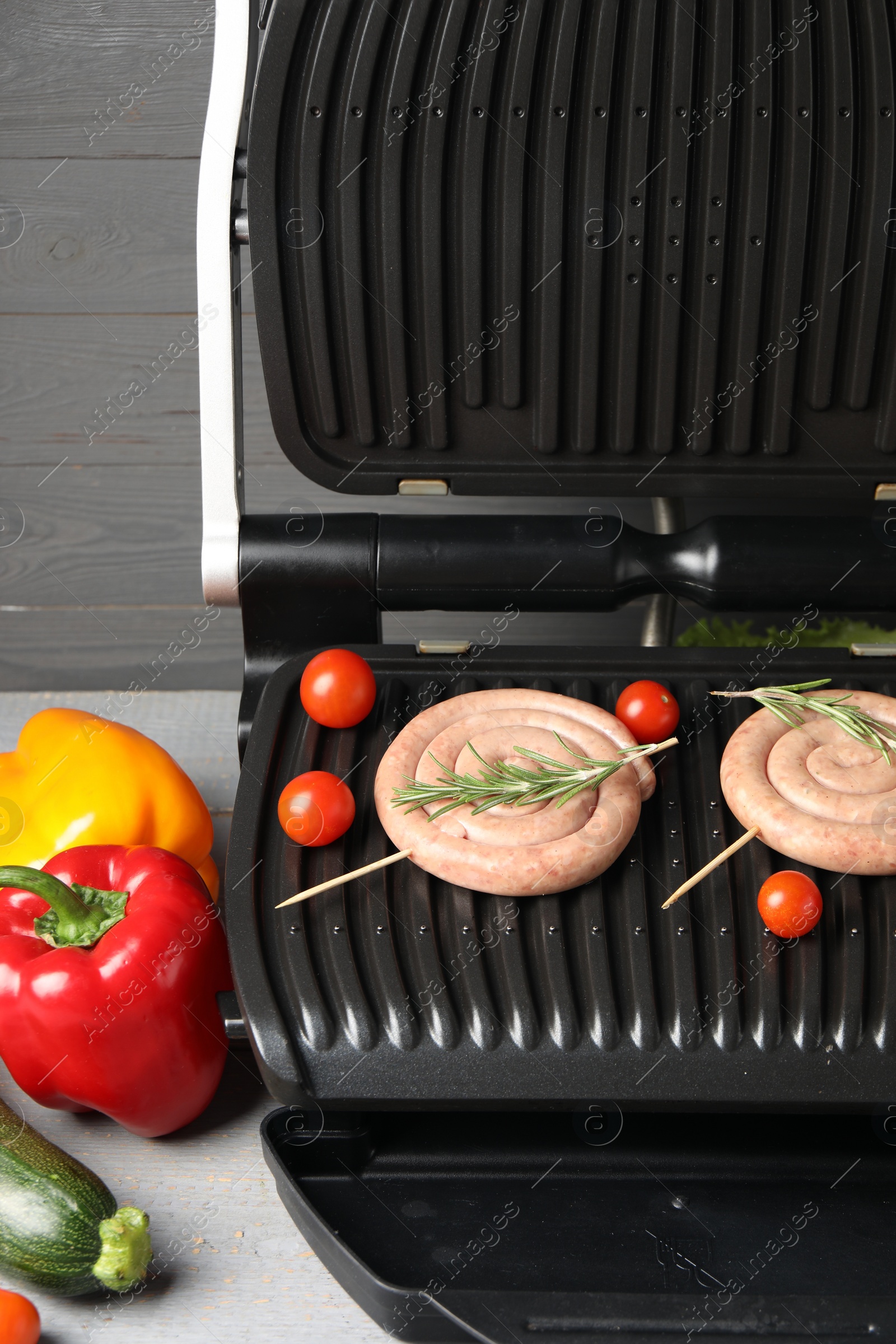 Photo of Electric grill with homemade sausages, rosemary and vegetables on table