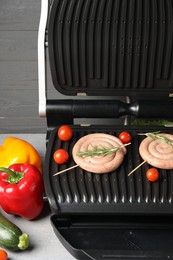 Photo of Electric grill with homemade sausages, rosemary and vegetables on table