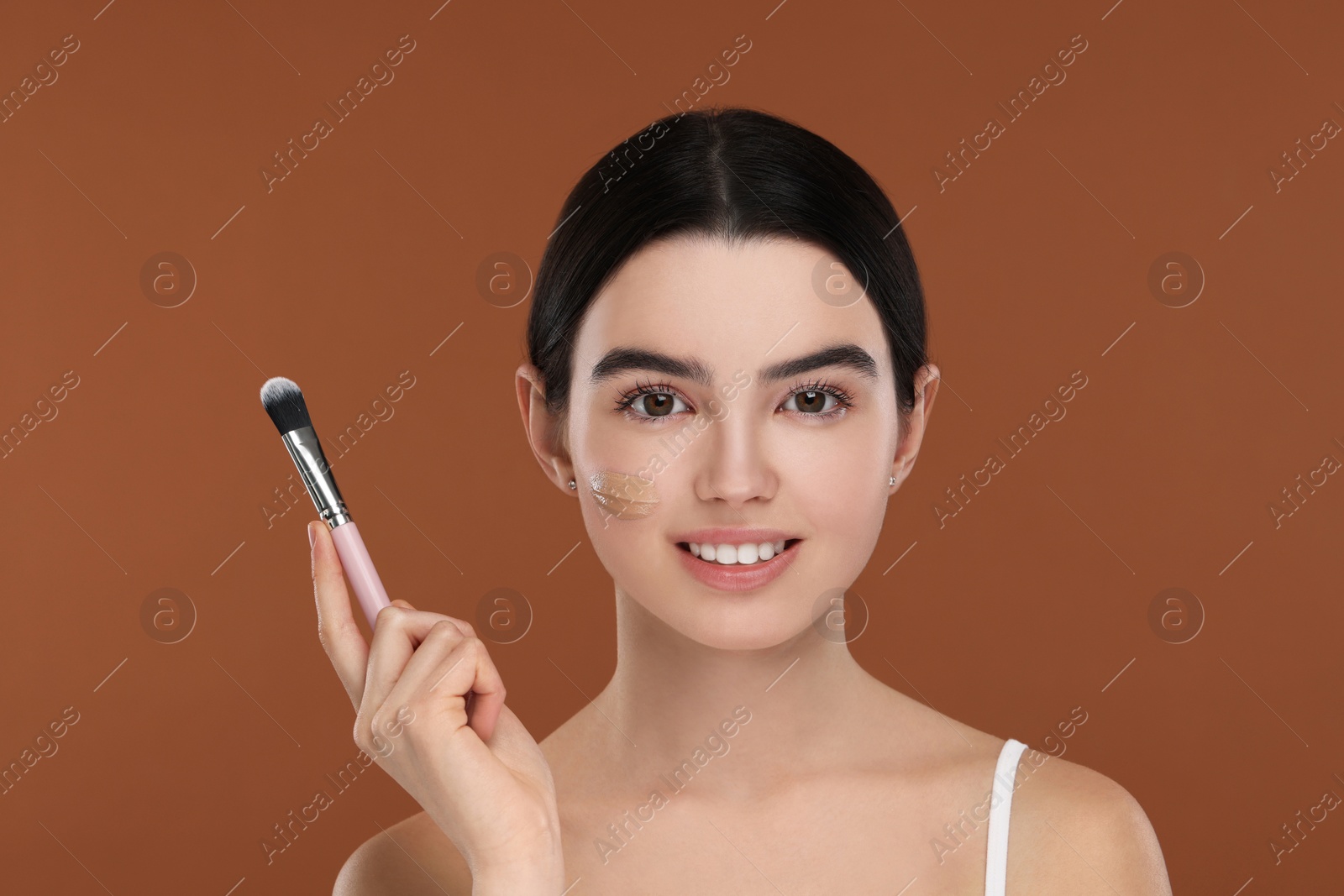 Photo of Teenage girl with swatch of foundation and makeup brush on brown background