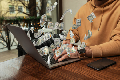 Image of Man with modern laptop and flying dollar banknotes at table indoors, closeup. People make money online