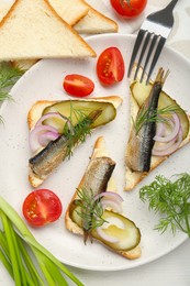 Photo of Delicious sandwiches with sprats, pickled cucumber, onion and dill served on white wooden table, flat lay