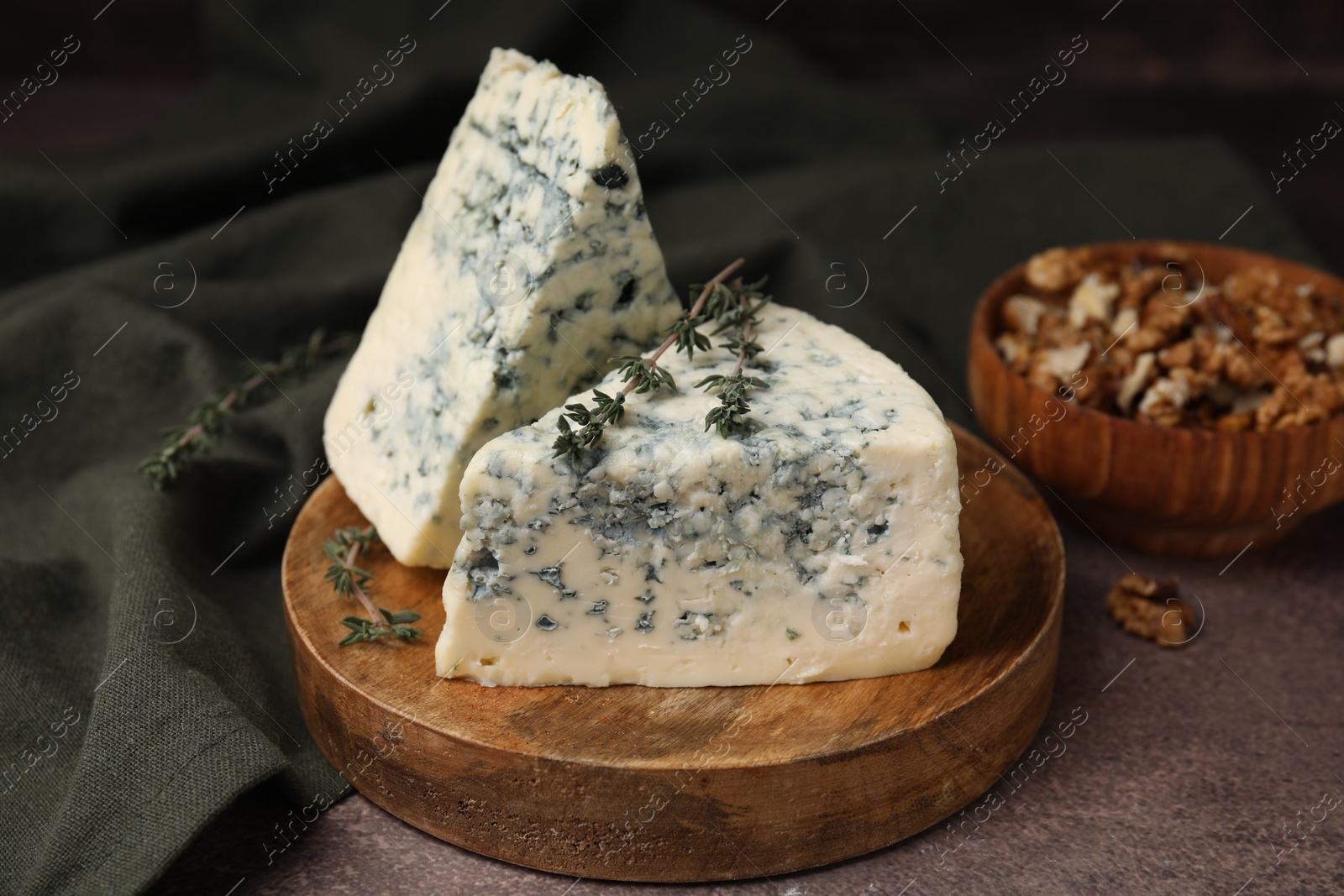 Photo of Tasty blue cheese with thyme and walnuts on brown table