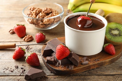 Photo of Fondue pot with chocolate and different products on wooden table