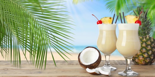 Tasty Pina Colada cocktail on wooden table near ocean, space for text. Banner design