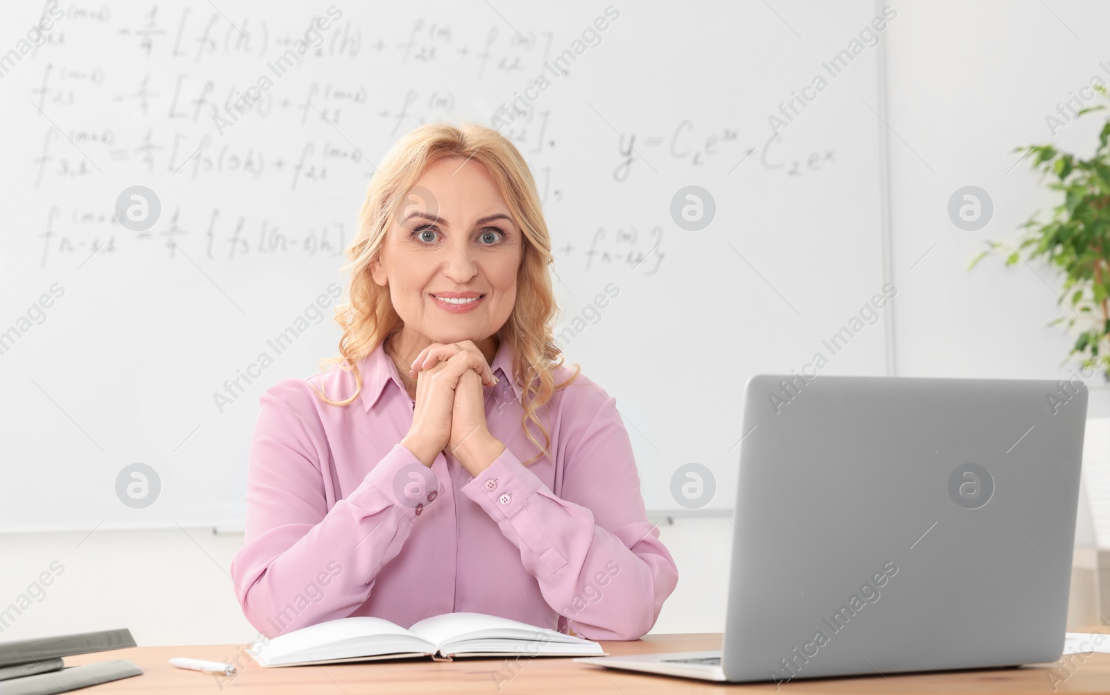 Photo of Happy teacher sitting near laptop at desk in classroom