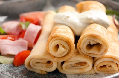 Photo of Thin pancakes with garnish on plate, closeup