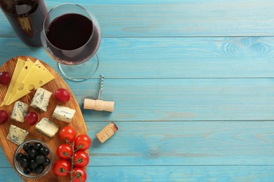 Tasty red wine and snacks on light blue wooden table, flat lay. Space for text