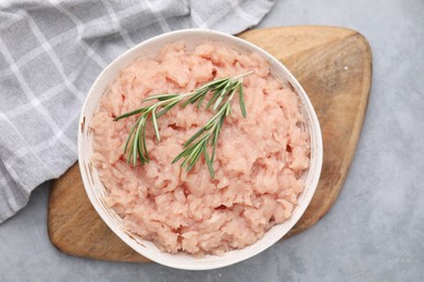 Photo of Fresh raw minced meat and rosemary in bowl on light grey textured table, top view