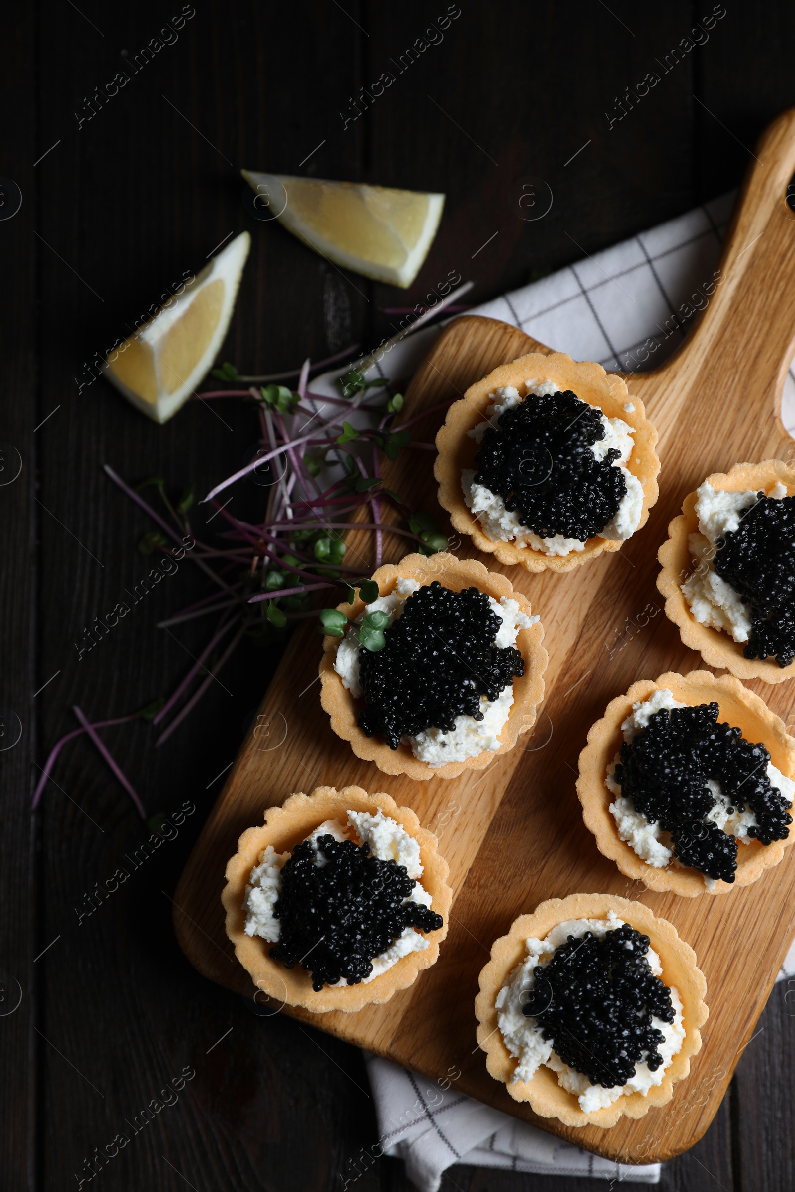 Photo of Board of delicious tartlets with black caviar and cream cheese on wooden table, top view