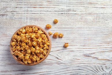 Photo of Delicious popcorn with caramel in bowl on wooden background, top view