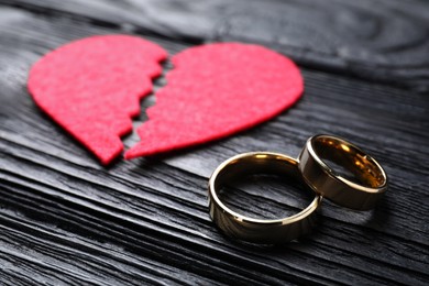 Photo of Divorce concept. Broken red paper heart and wedding rings on black wooden table, closeup