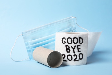 Photo of Toilet paper roll with text Goodbye 2020 and medical face mask on light blue background