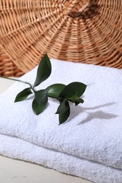 Stacked terry towels and green branch on white table, closeup