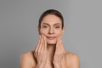 Photo of Woman massaging her face on grey background