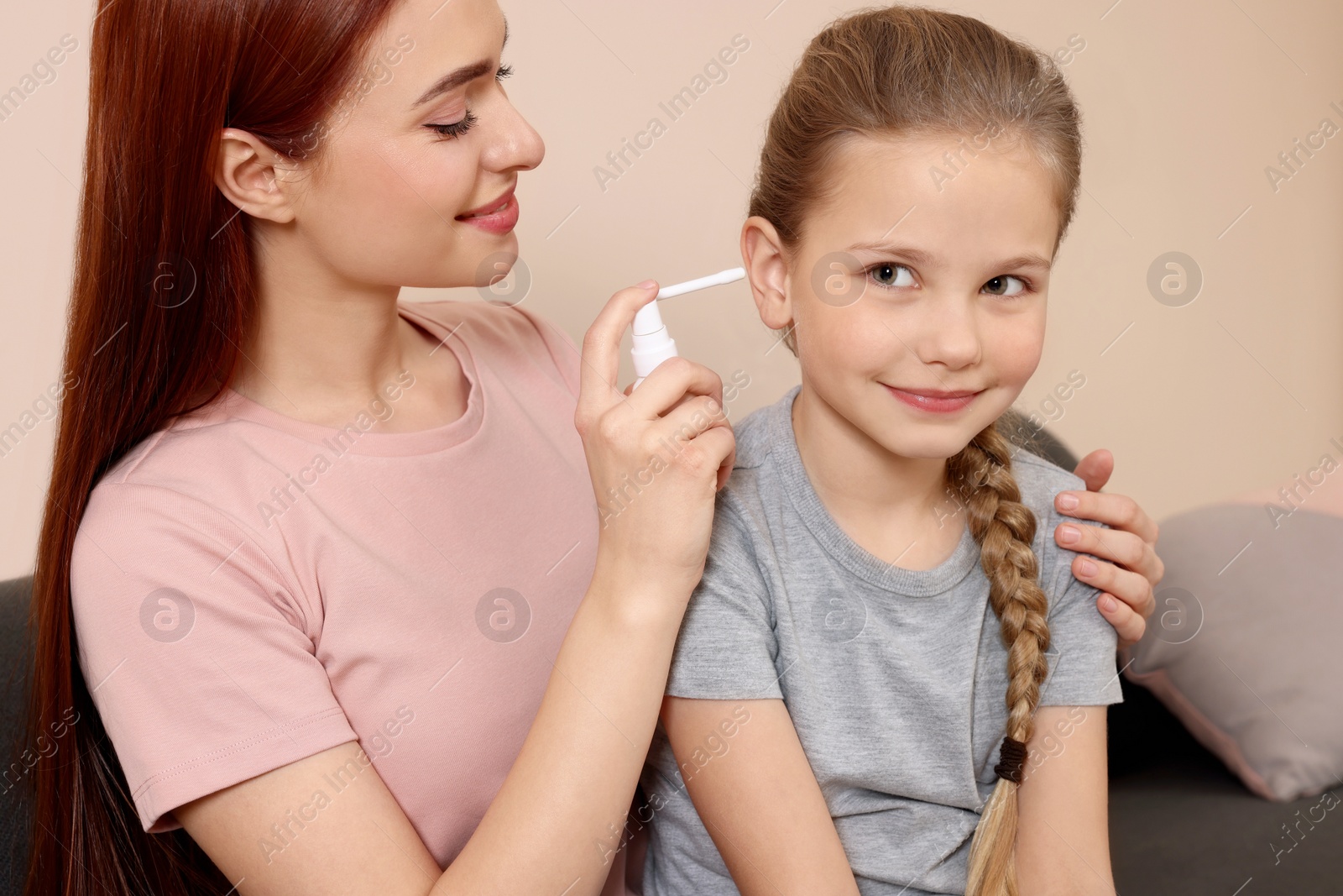 Photo of Mother spraying medication into daughter's ear in living room